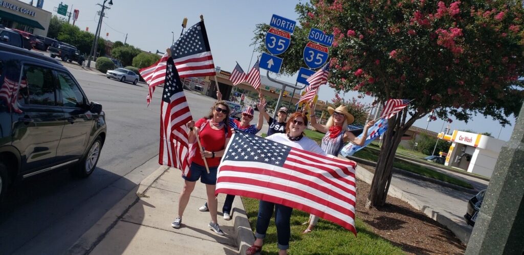 A group of people holding american flags on the side walk
