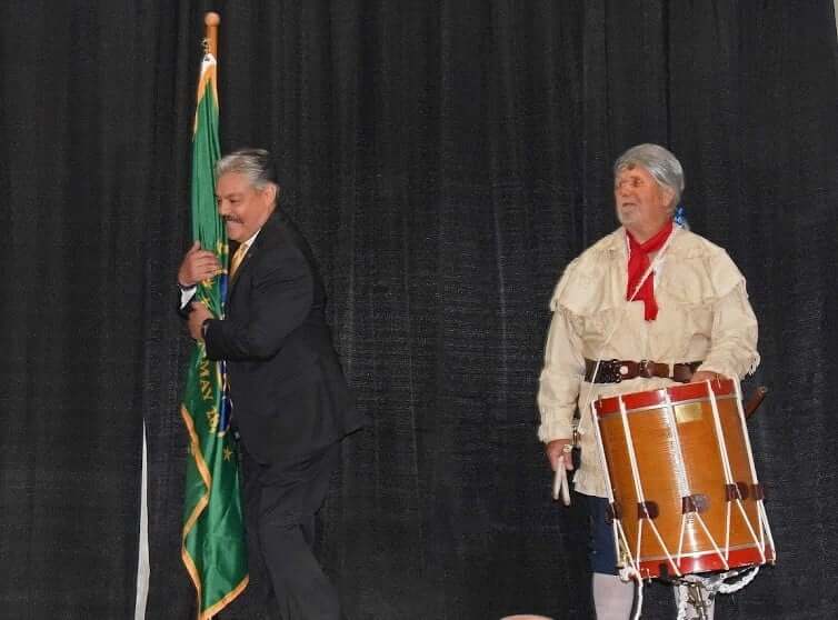 Two men in costumes are playing drums and a flag.