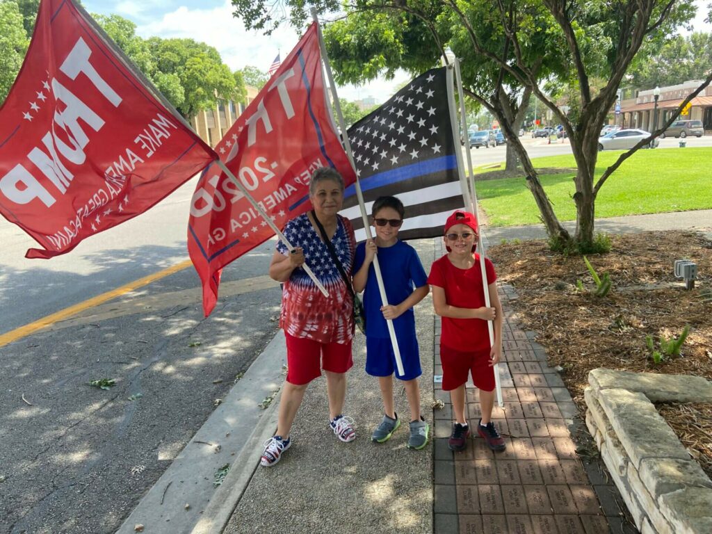 Three children holding flags on a sidewalk.