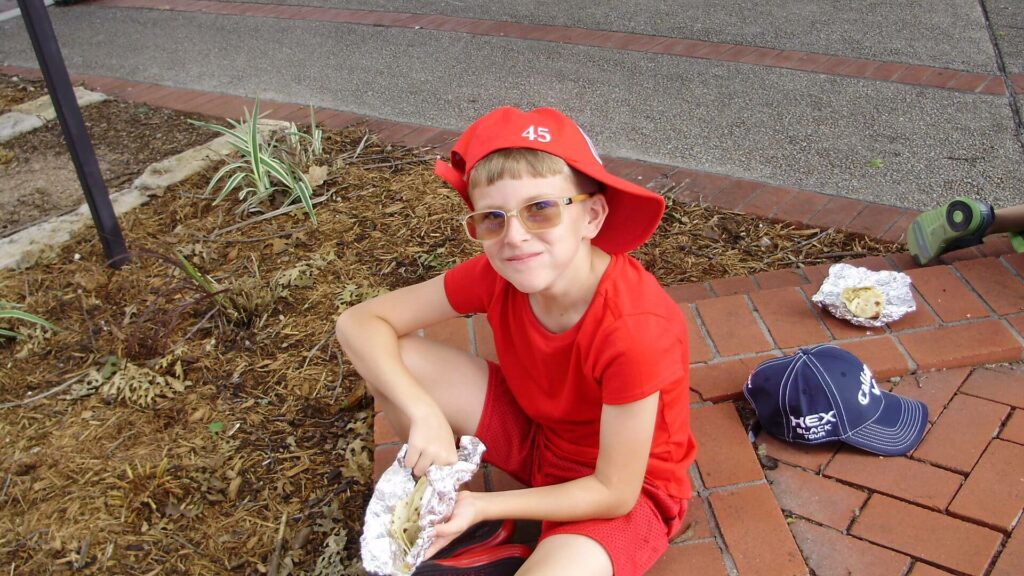 A boy in red shirt sitting on ground holding food.