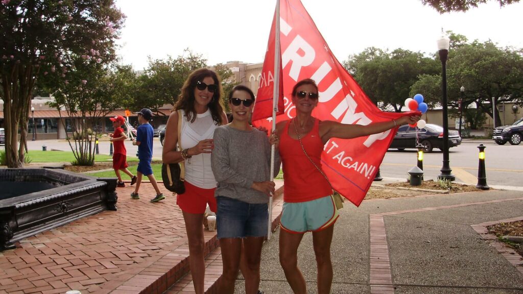 Three women standing next to each other holding a red flag.