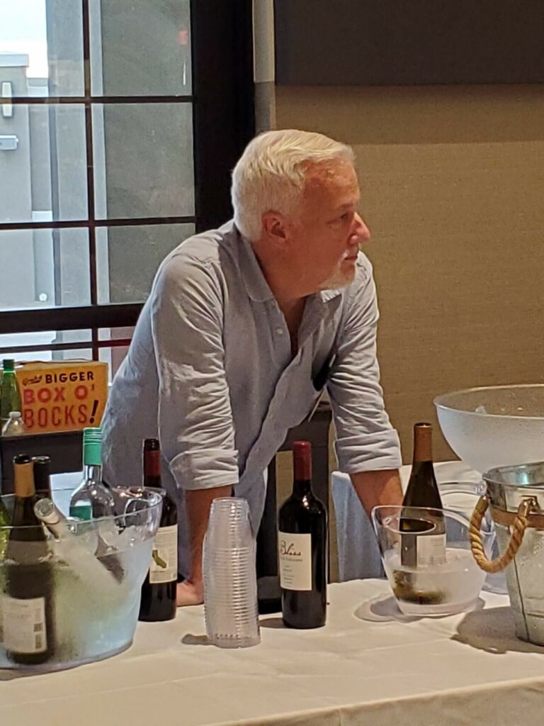 A man standing at the table with several bottles of wine.