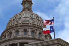 A flag flies in front of the texas state capitol building.