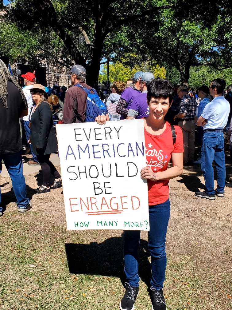 A woman holding up a sign that says " every american should be enraged ".