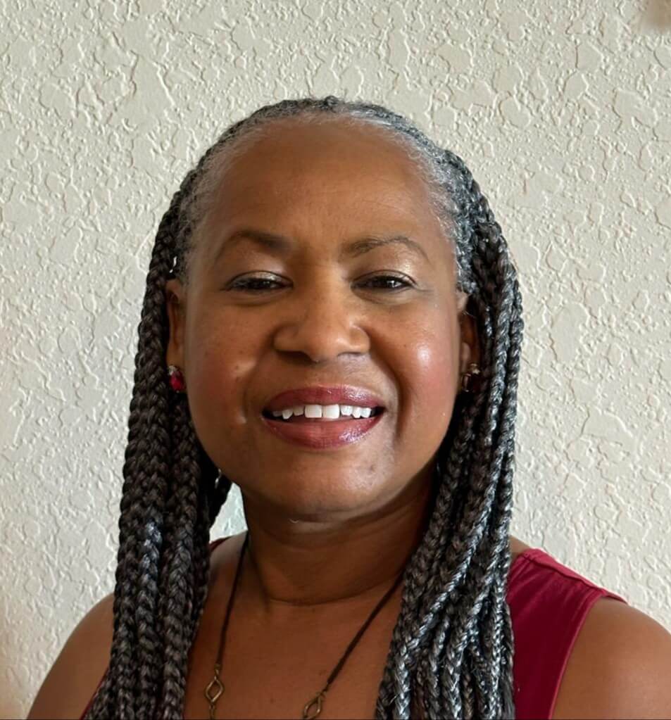 A smiling woman with braided hair against a textured wall.