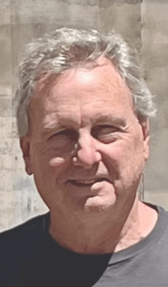 A smiling middle-aged man with graying hair outdoors.